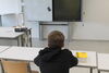 Junge sitzt an einem Schreibpult in der Schule. Einen Duden hat er neben sich auf dem Tisch liegen.