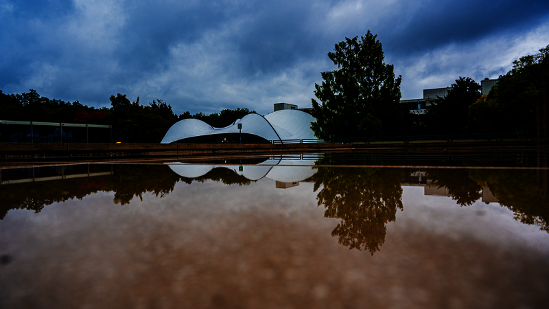Ein Panoramabild der Pädagogischen Hochschule mit Blick auf die Zeltkonstruktion Spinne. Im Vordergrund spiegelt sich das Zelt im Wasser.