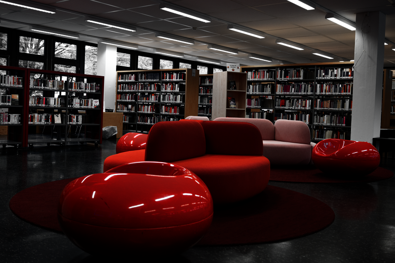 Das Bild zeigt eine Sietzgruppe in der Bibliothek der Pädagogischen Hochschule. Die Farben sind fast alle sehr gedämpft und ausgegraut, bis auf die knalligen Rottöne der Sitzgruppe. 