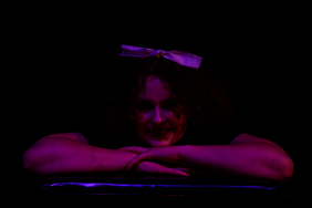 Frau im Magenta Cosplay, den Kopf auf die Arme abgelegt, grinsend 